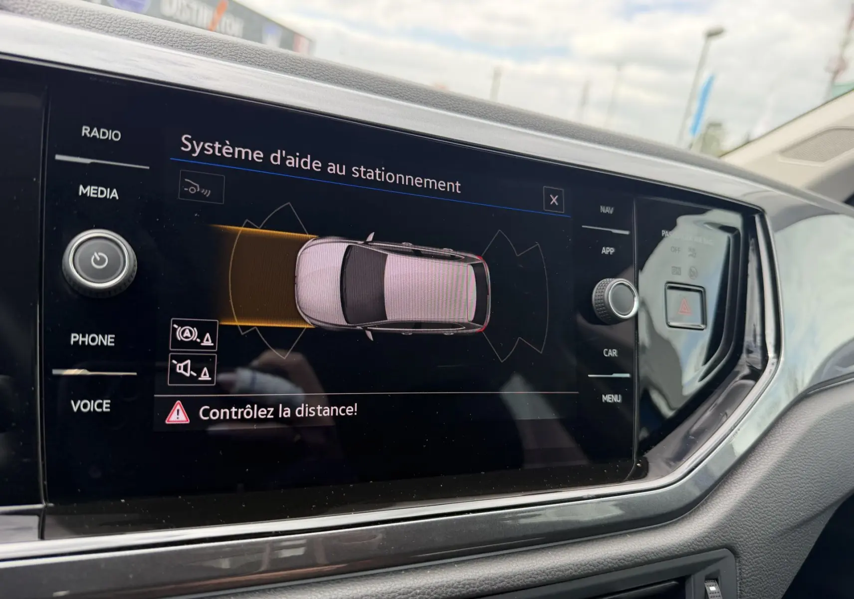 Écran tactile intérieur montrant l'aide au stationnement d'une Volkswagen Polo 2025, vue de face côté conducteur.