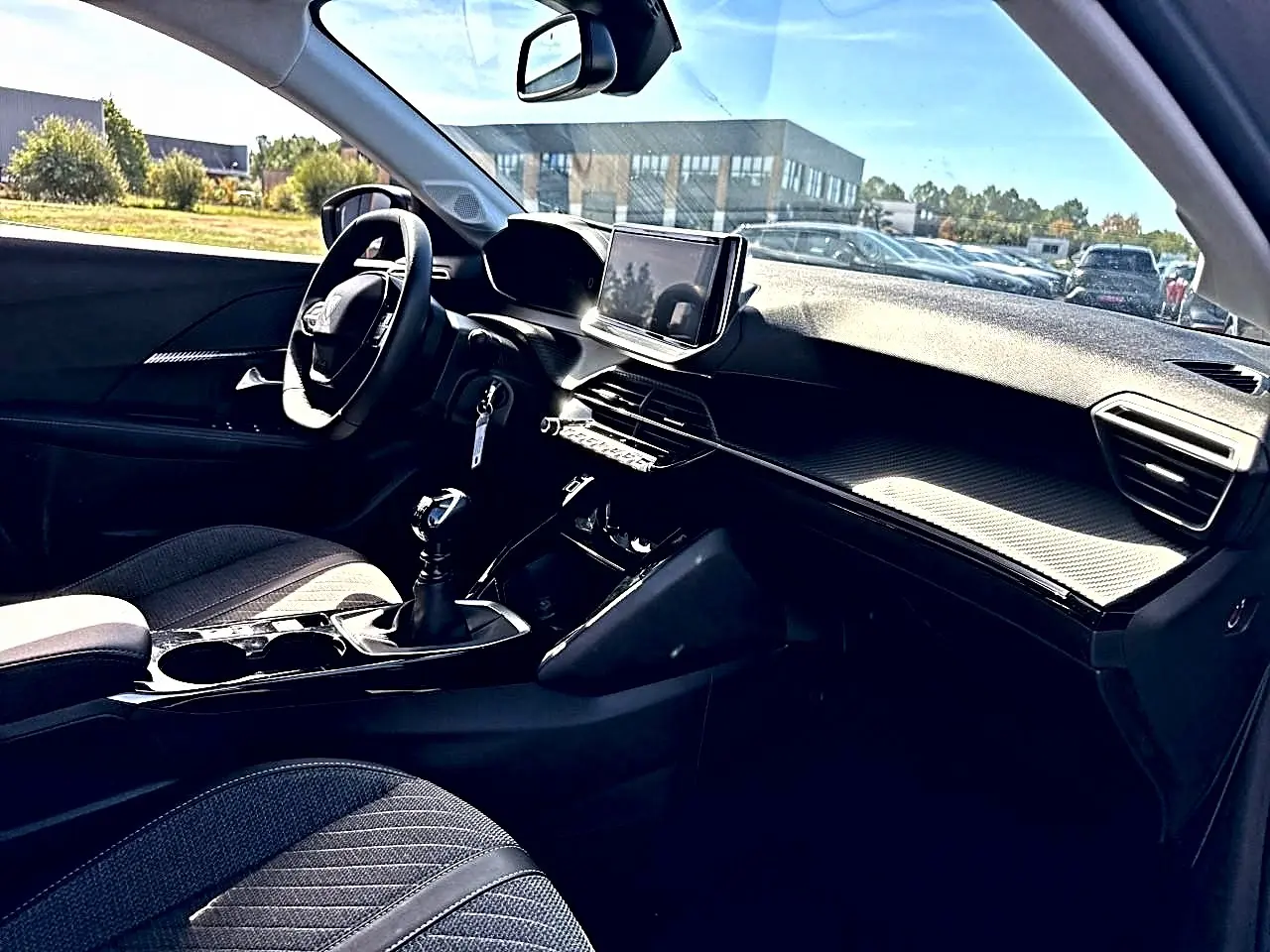 Intérieur de la Peugeot 208 1.2 100 Allure, vue côté conducteur, tableau de bord moderne avec écran tactile et volant noir.
