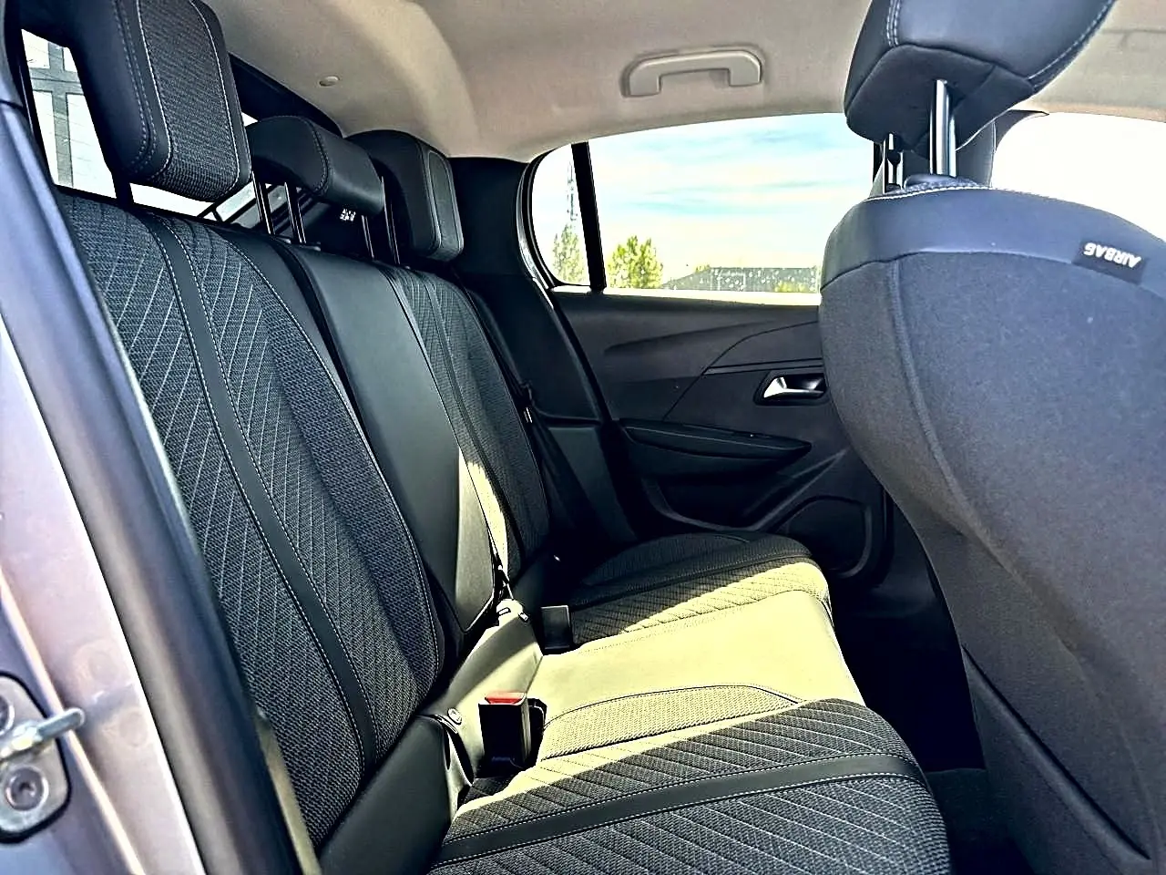 Vue intérieure côté gauche des sièges arrière gris foncé de la Peugeot 208 1.2 100 allure avec appuie-têtes et ceintures visibles.