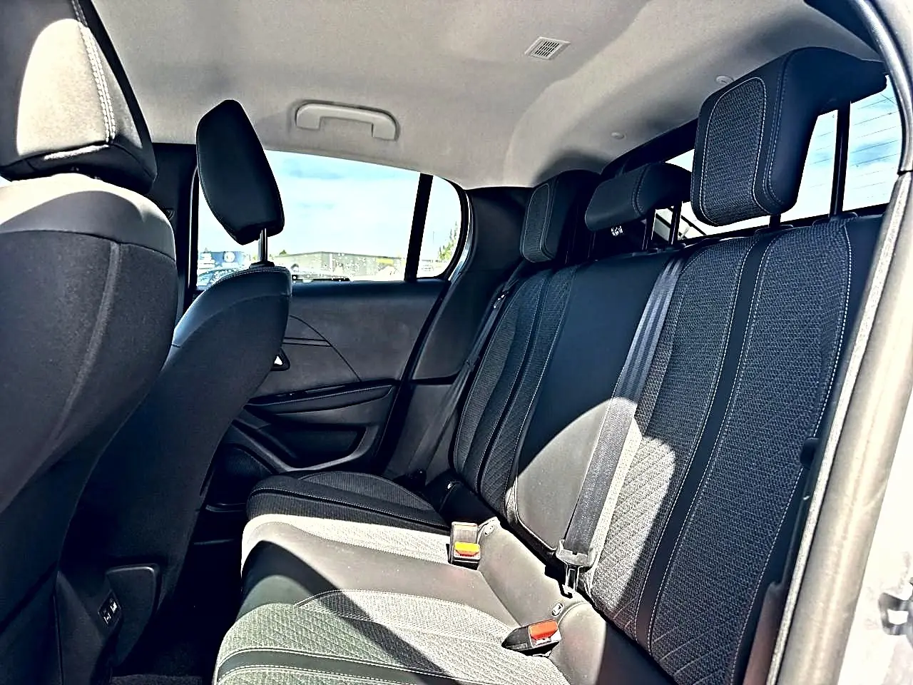 Vue intérieure arrière de la Peugeot 208 1.2 100 Allure avec sièges tissu gris et ceintures de sécurité visibles.