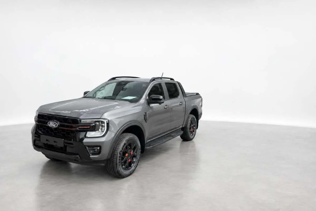 Ford Ranger Wildtrak gris carbone en 3/4 avant droit, avec jantes noires et barres de toit visibles.