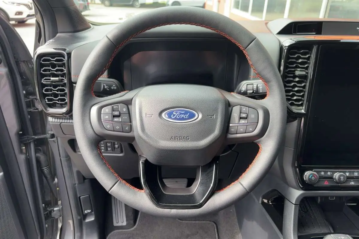 Vue rapprochée du volant cuir noir avec surpiqûres orange du Ford Ranger Wildtrak Plus 2026, tableau de bord partiel visible.