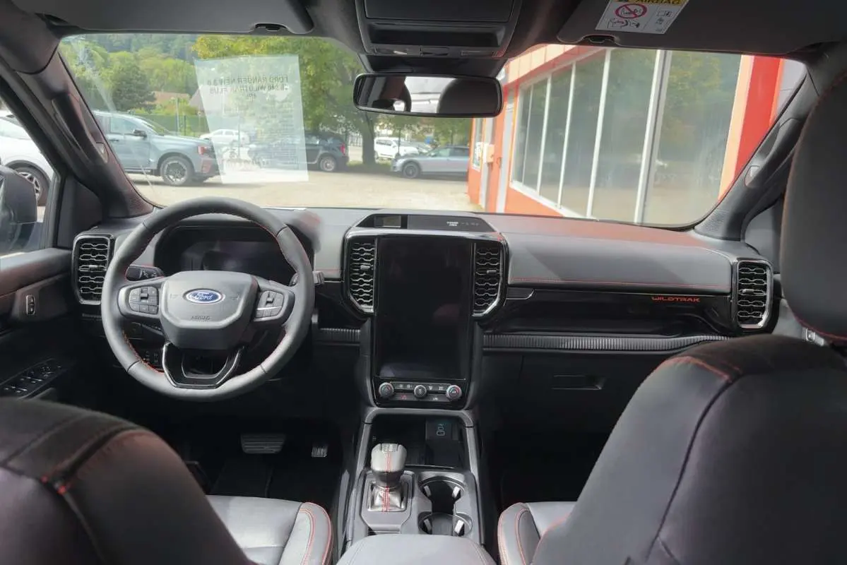 Vue intérieure avant du Ford Ranger Wildtrak 2026 avec tableau de bord noir, écran central vertical et volant cuir multifonctions.