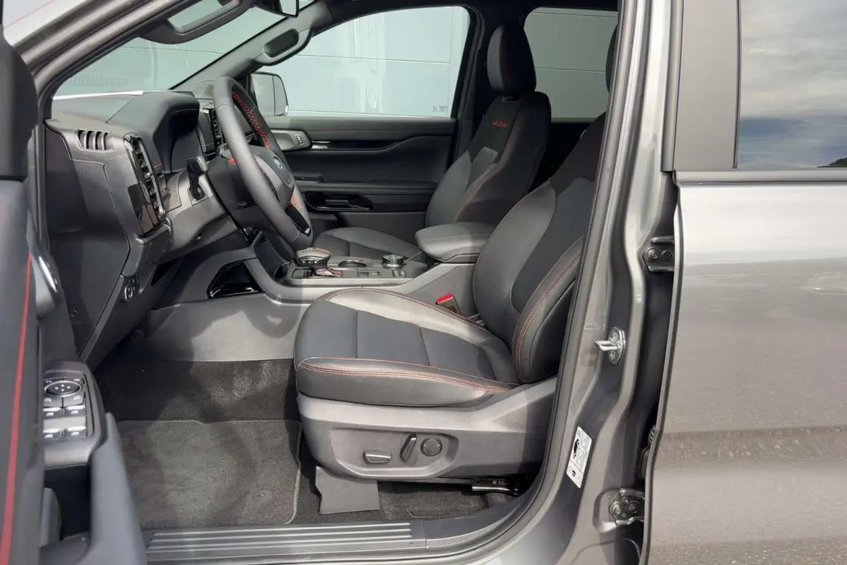 Vue intérieure côté conducteur du Ford Ranger gris carbone 2026, sièges noirs avec surpiqûres rouges et tableau de bord moderne.