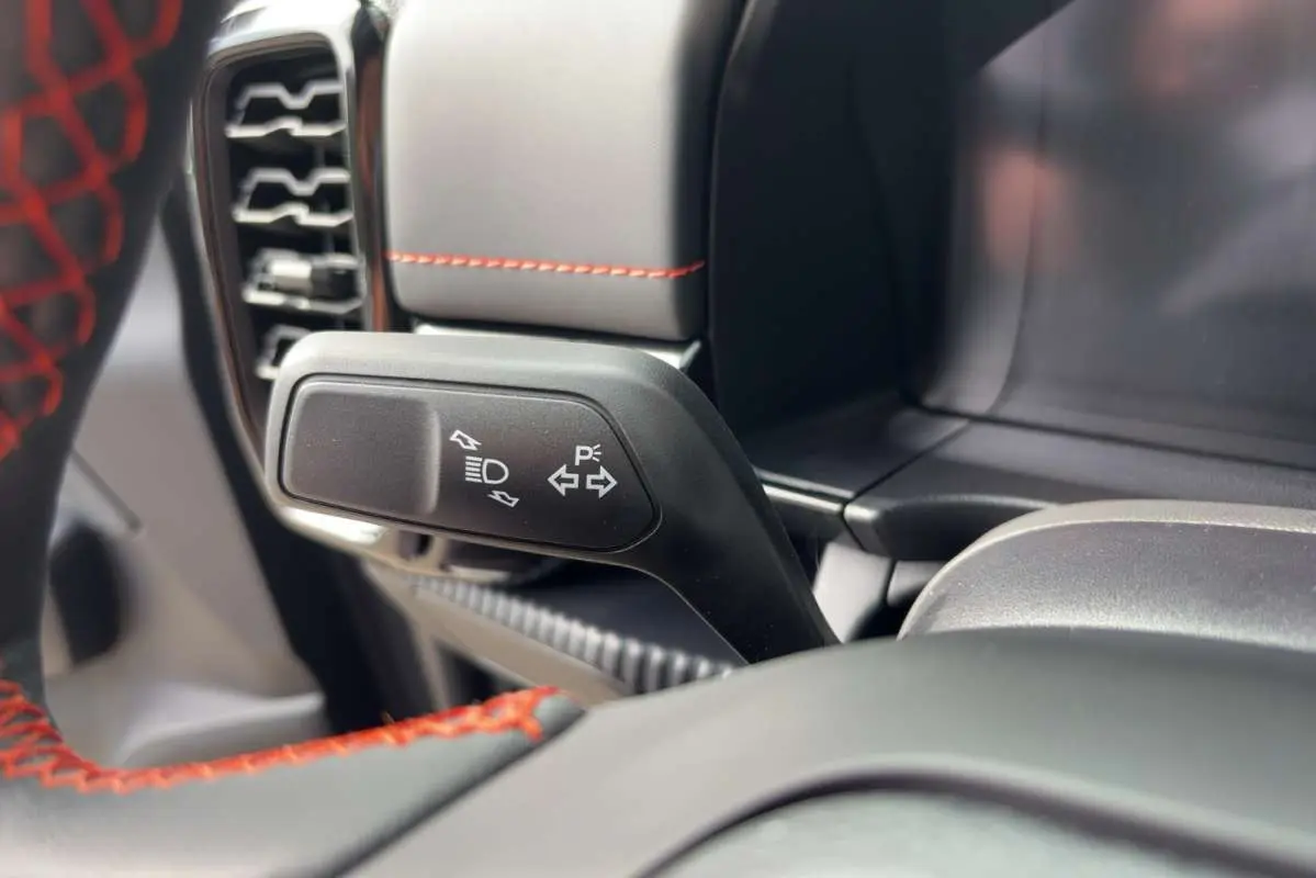 Gros plan sur la manette de clignotant noire avec pictogrammes blancs, volant noir avec surpiqûres rouges dans un Ford Ranger gris carbone.