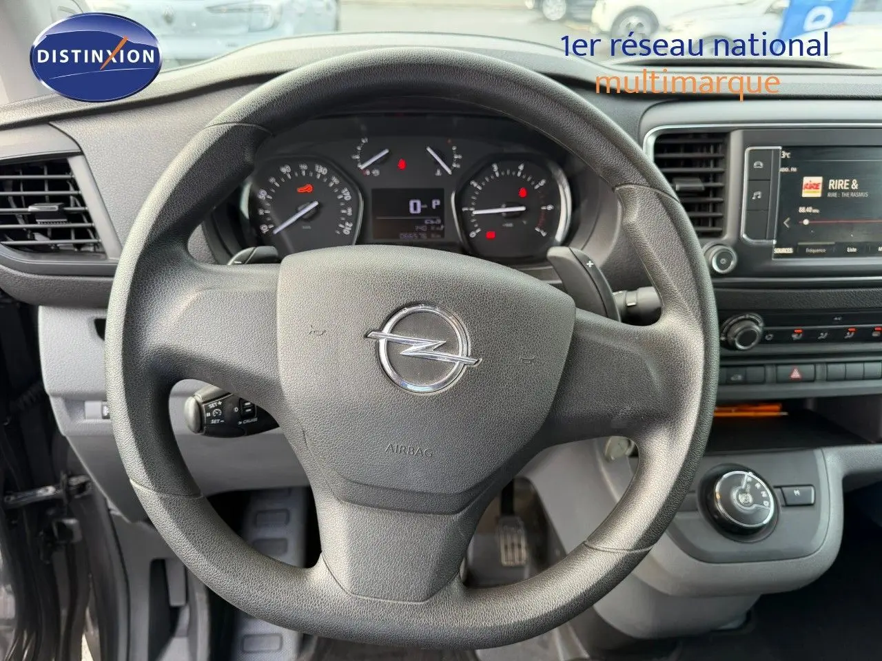 Vue intérieure centrée sur le volant Opel du Vivaro Fourgon gris Pierre de Lune, tableau de bord et écran multimédia visibles.