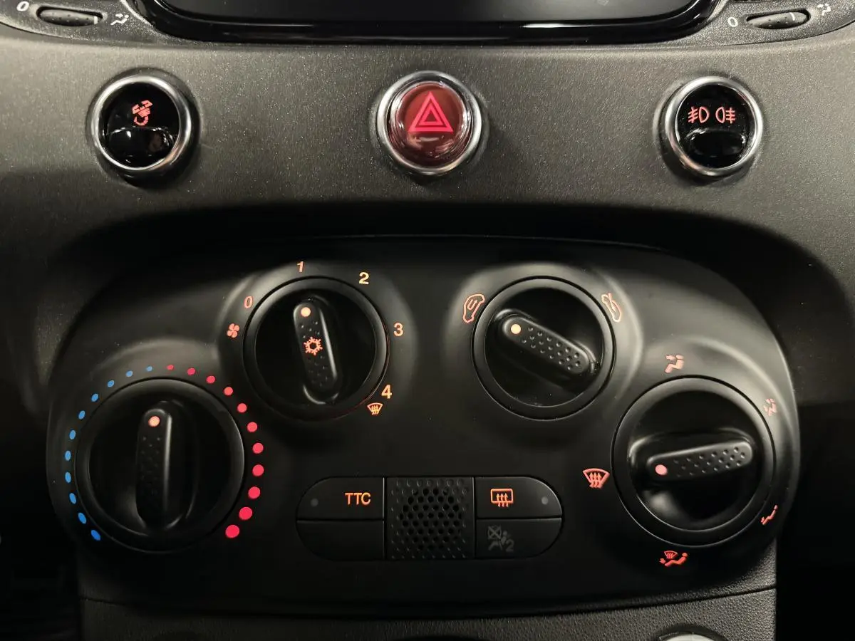 Vue rapprochée du tableau de bord noir de l'Abarth 595 Competizione avec commandes de climatisation et bouton TTC éclairés.
