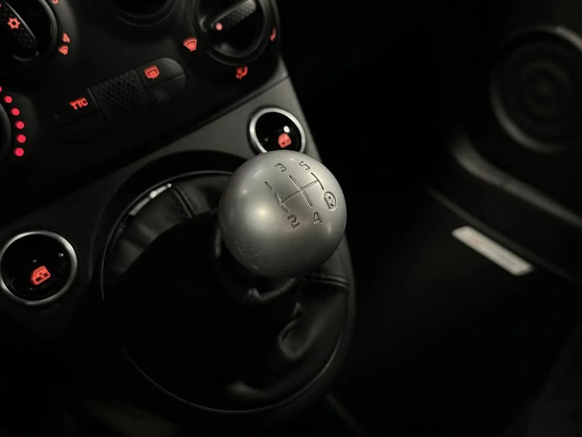 Gros plan sur le pommeau de levier de vitesses aluminium de l'ABARTH 595 Competizione noir, avec commandes éclairées rouges.