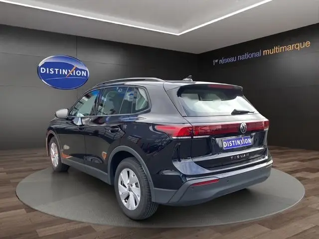 Vue 3/4 arrière droite d’un Volkswagen Tiguan noir 2024 dans un showroom avec logo Distinxion en arrière-plan.