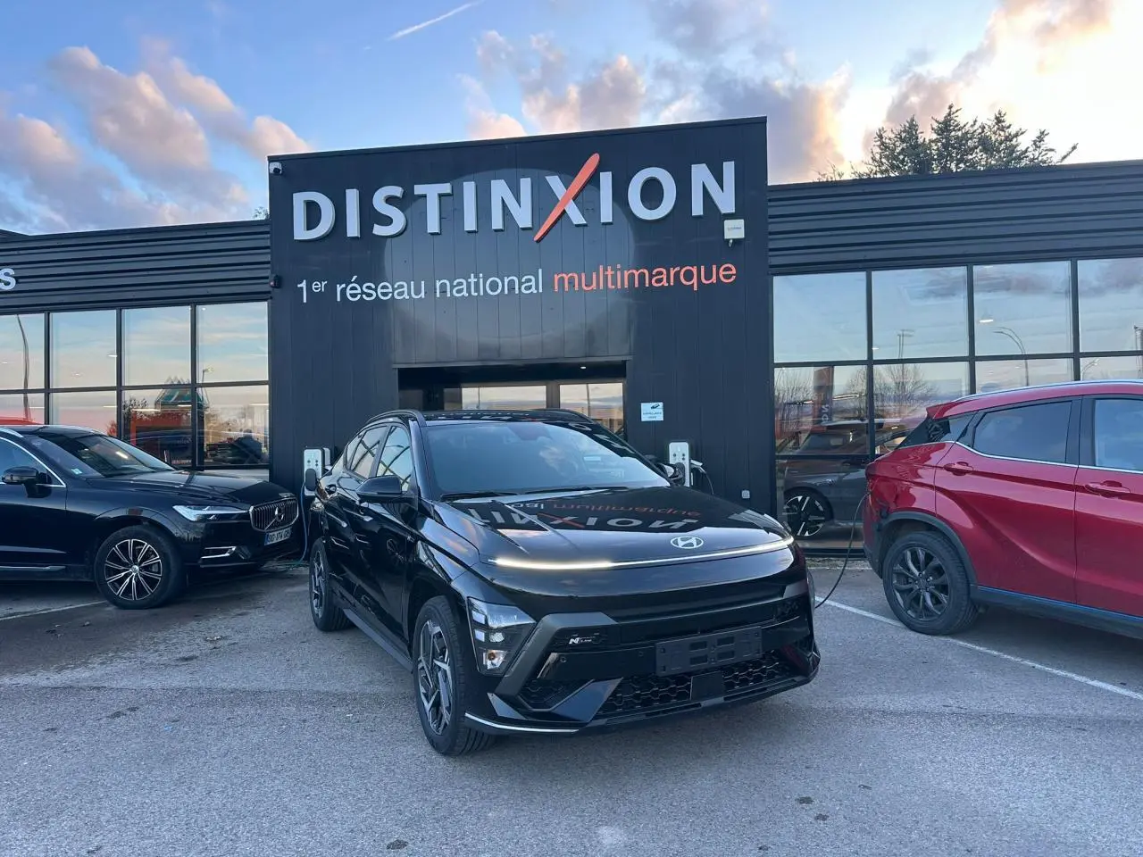 Vue 3/4 avant d'un Hyundai KONA II noir Abyss Metal avec jantes alliage et calandre marquée N Line, stationné devant un bâtiment Distinxion.