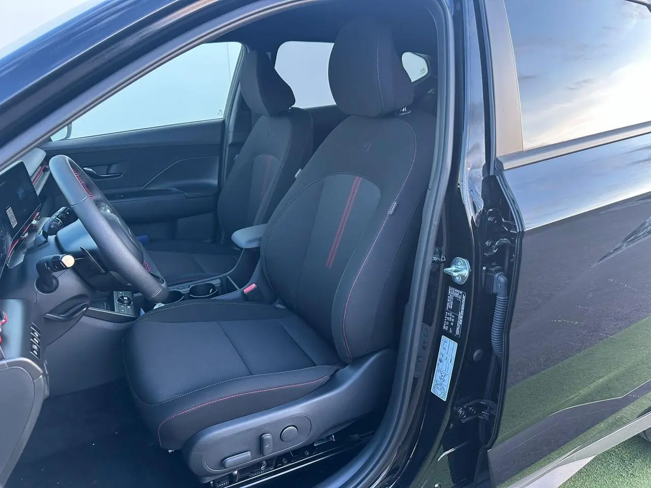 Vue intérieure côté conducteur du Hyundai KONA II noir Abyss Metal, sièges N Line avec surpiqûres rouges et volant cuir.