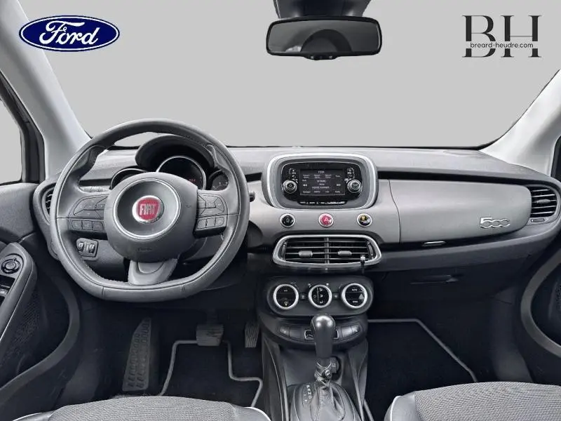 Vue intérieure avant du tableau de bord gris et noir d'une Fiat 500X 1.4 MultiAir avec volant multifonction et écran tactile central.