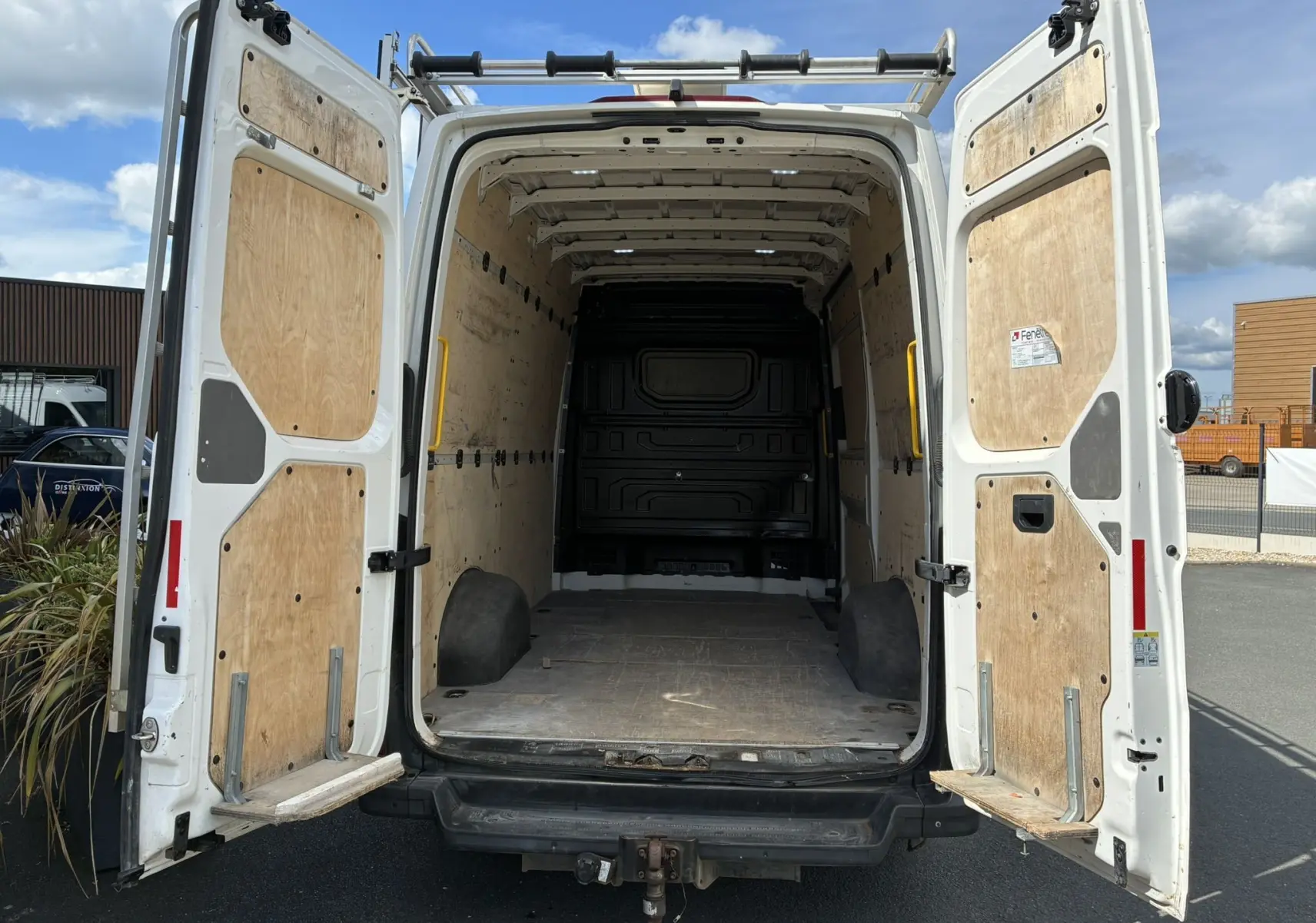 Vue arrière ouverte du Volkswagen Crafter blanc, montrant l'intérieur vide avec parois et plancher en bois.