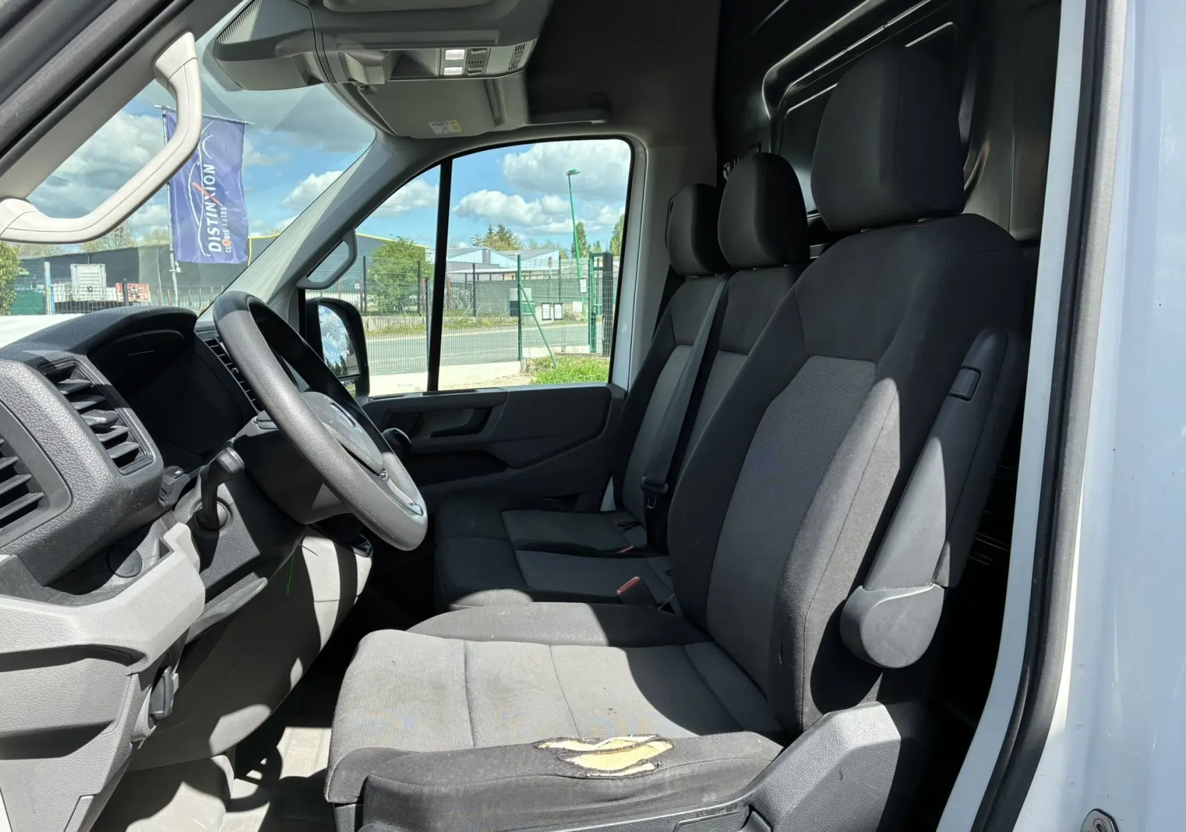 Vue intérieure côté conducteur du Volkswagen Crafter blanc, montrant la banquette avant noire et le tableau de bord.