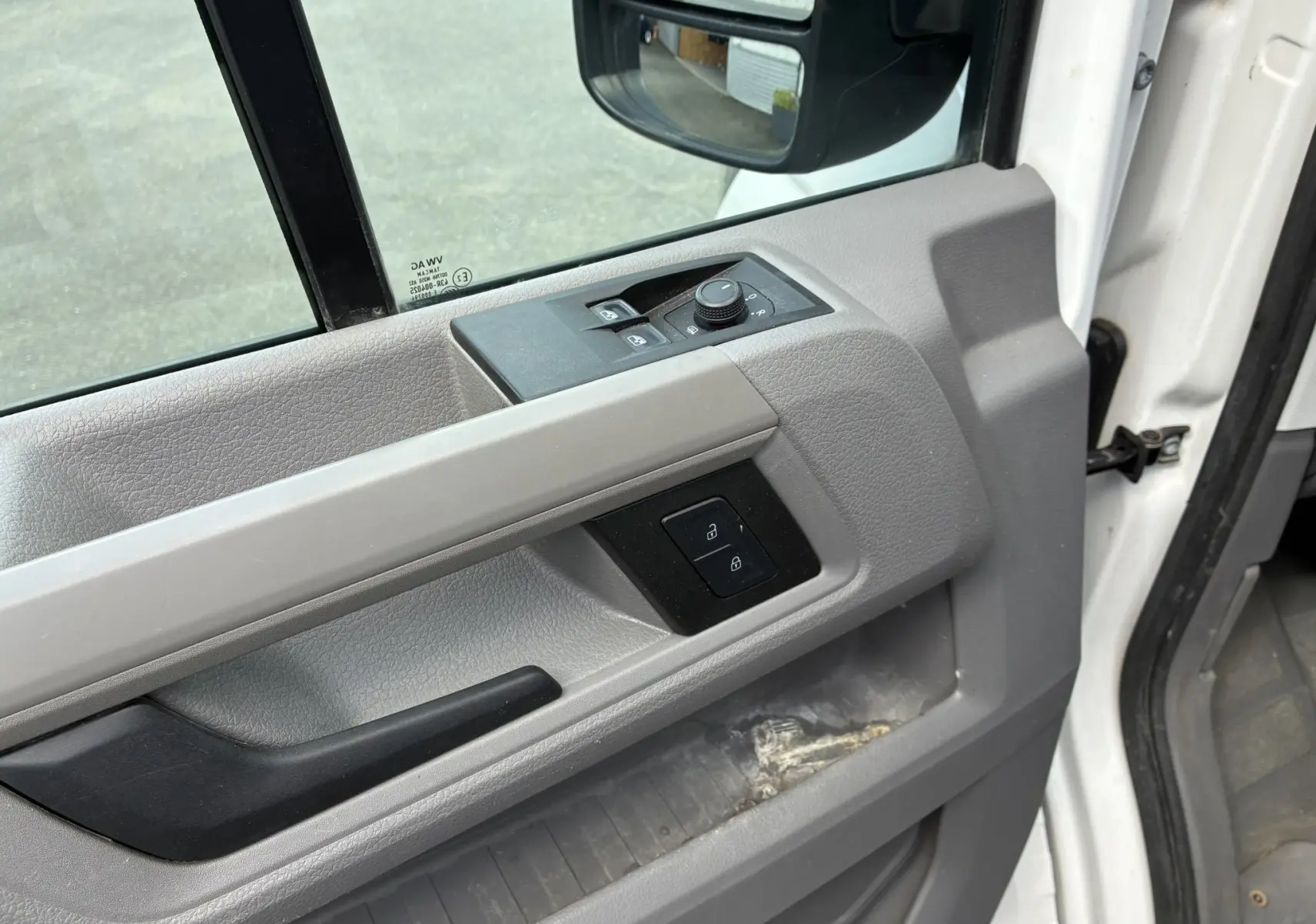 Vue rapprochée de la porte conducteur grise du Volkswagen Crafter blanc, avec commandes électriques et rétroviseur visible.