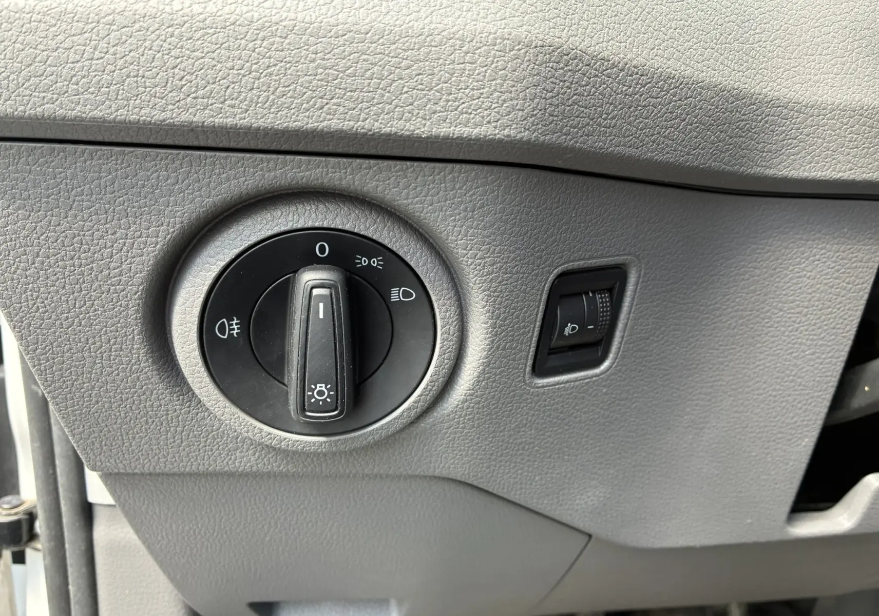 Gros plan sur le bouton de commande des phares et le réglage d’intensité lumineuse dans un Volkswagen Crafter blanc.
