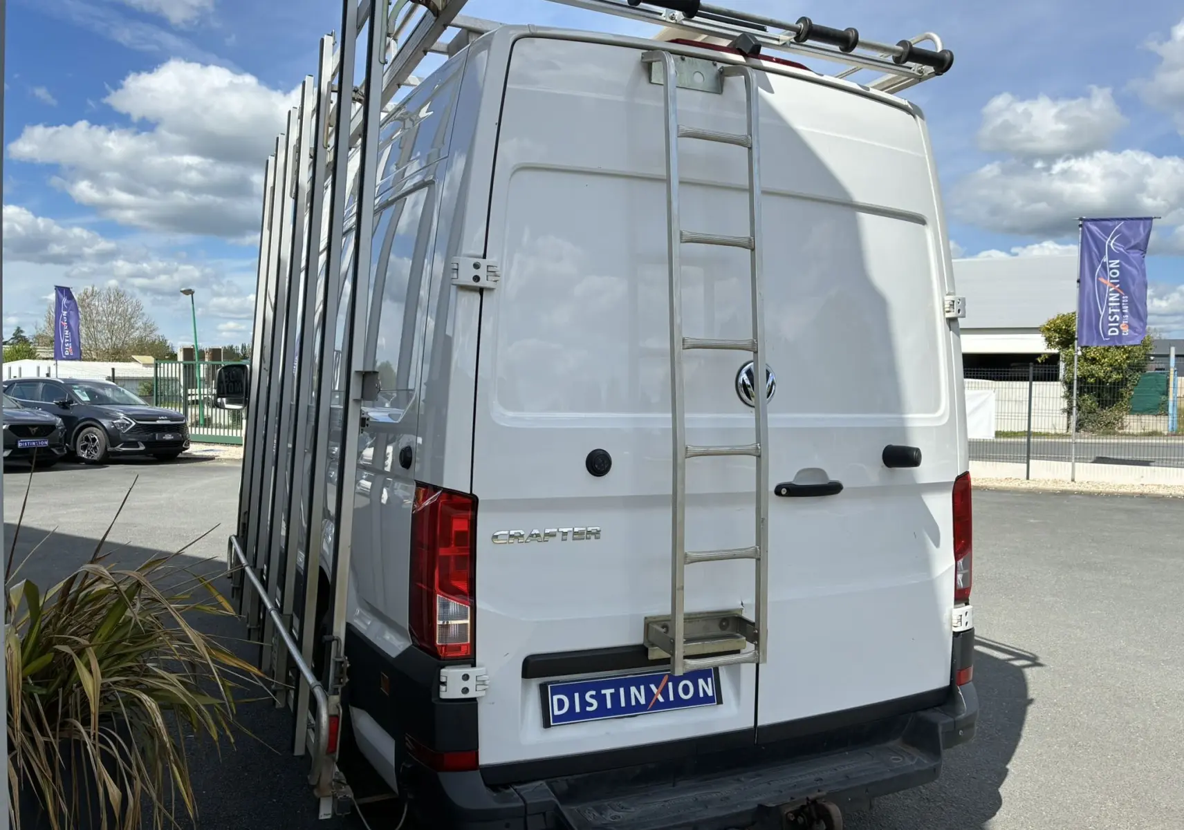 Vue arrière d’un Volkswagen Crafter blanc avec échelle métallique et porte-outils sur le côté droit.