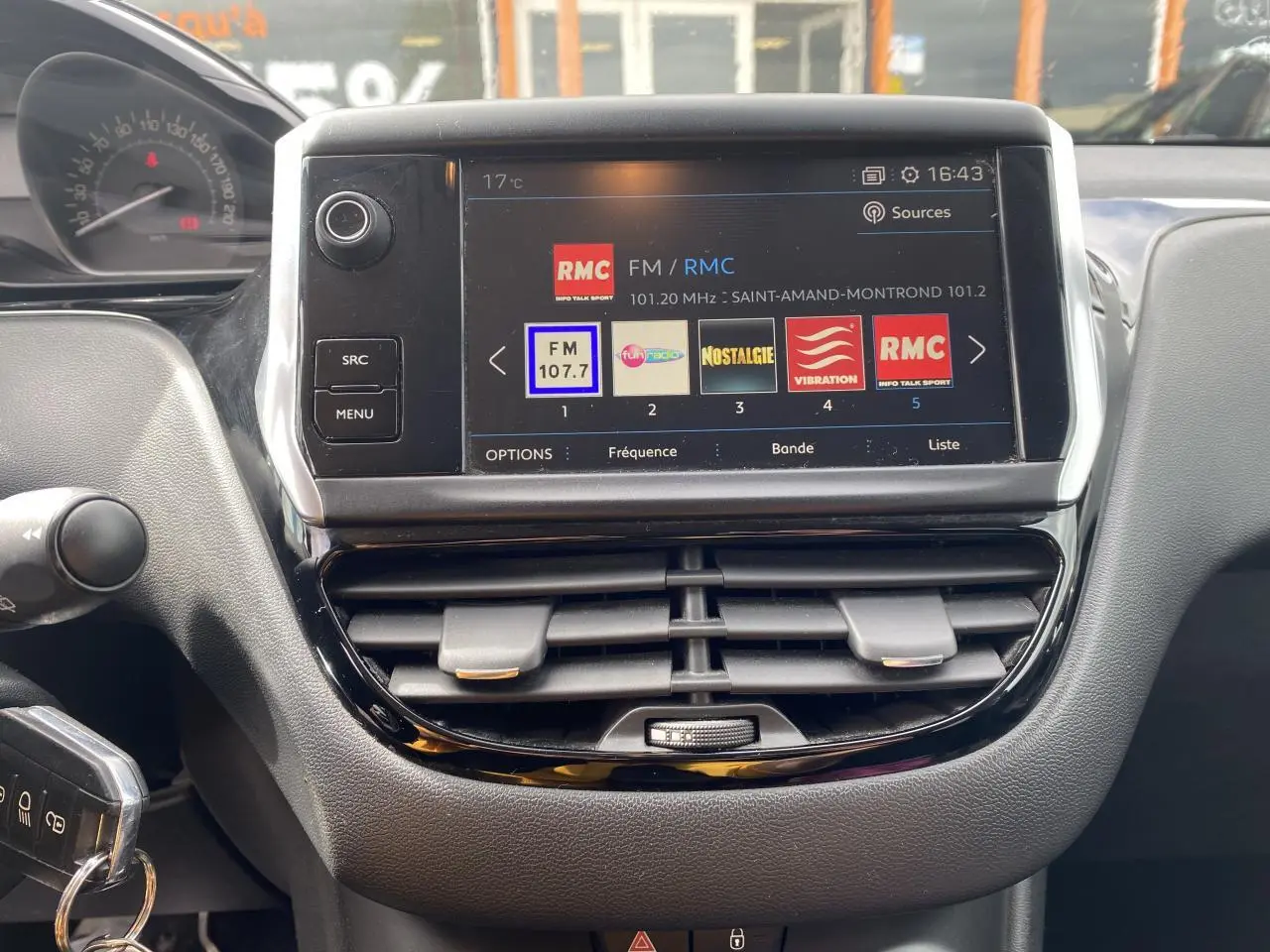 Vue rapprochée de l’écran tactile central et tableau de bord de la Peugeot 208 gris, avec affichage radio FM et commandes autour.