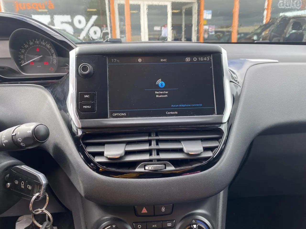 Vue rapprochée du tableau de bord de la Peugeot 208 gris, avec écran tactile central affichant la recherche Bluetooth.