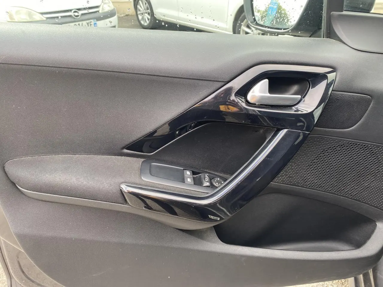 Gros plan sur la contre-porte avant gauche noire avec commandes des vitres électriques et poignée brillante.