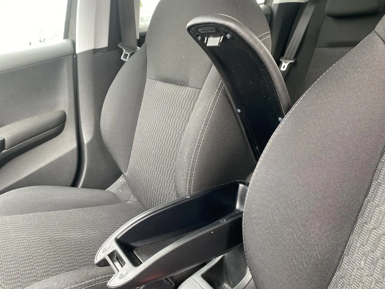 Vue intérieure rapprochée du siège avant droit d'une Peugeot 208 gris, avec accoudoir central ouvert et tissu texturé.