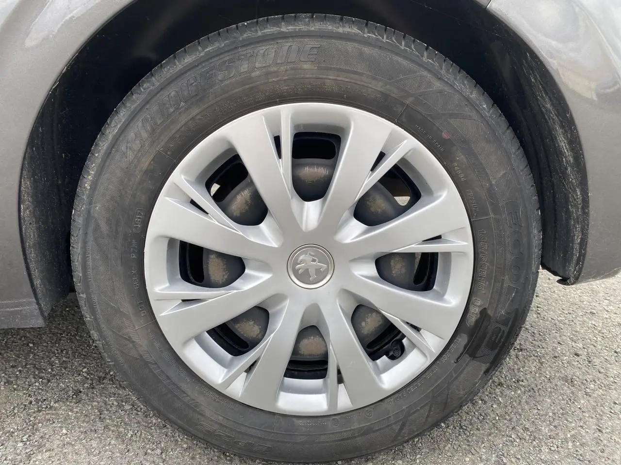 Gros plan sur la roue avant droite d’une Peugeot 208 gris métallisé, avec enjoliveur argenté et logo Peugeot central.