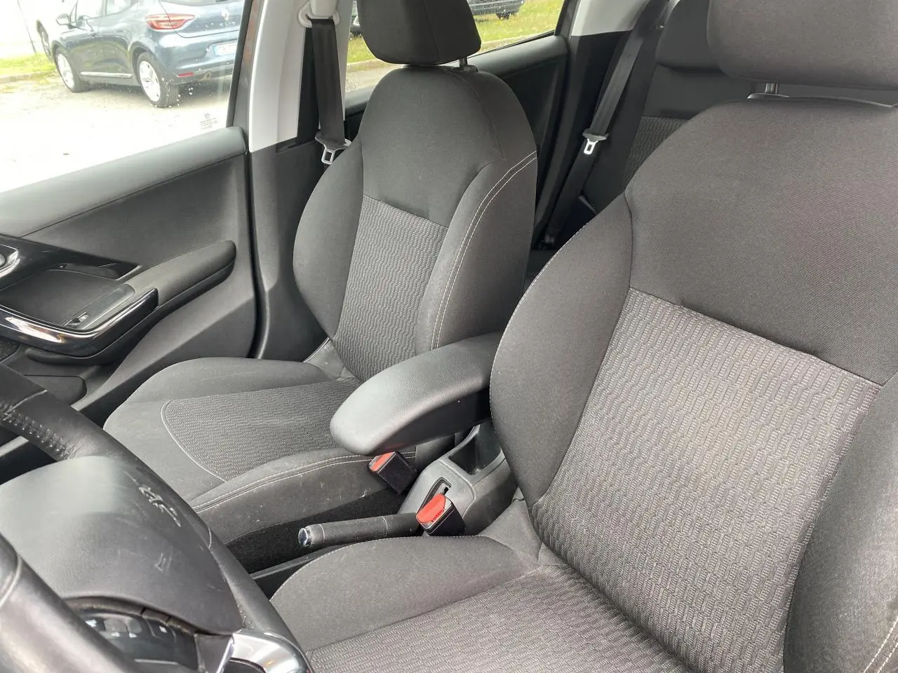 Vue intérieure de la Peugeot 208 gris, montrant les sièges avant avec accoudoir central et partie du volant côté gauche.