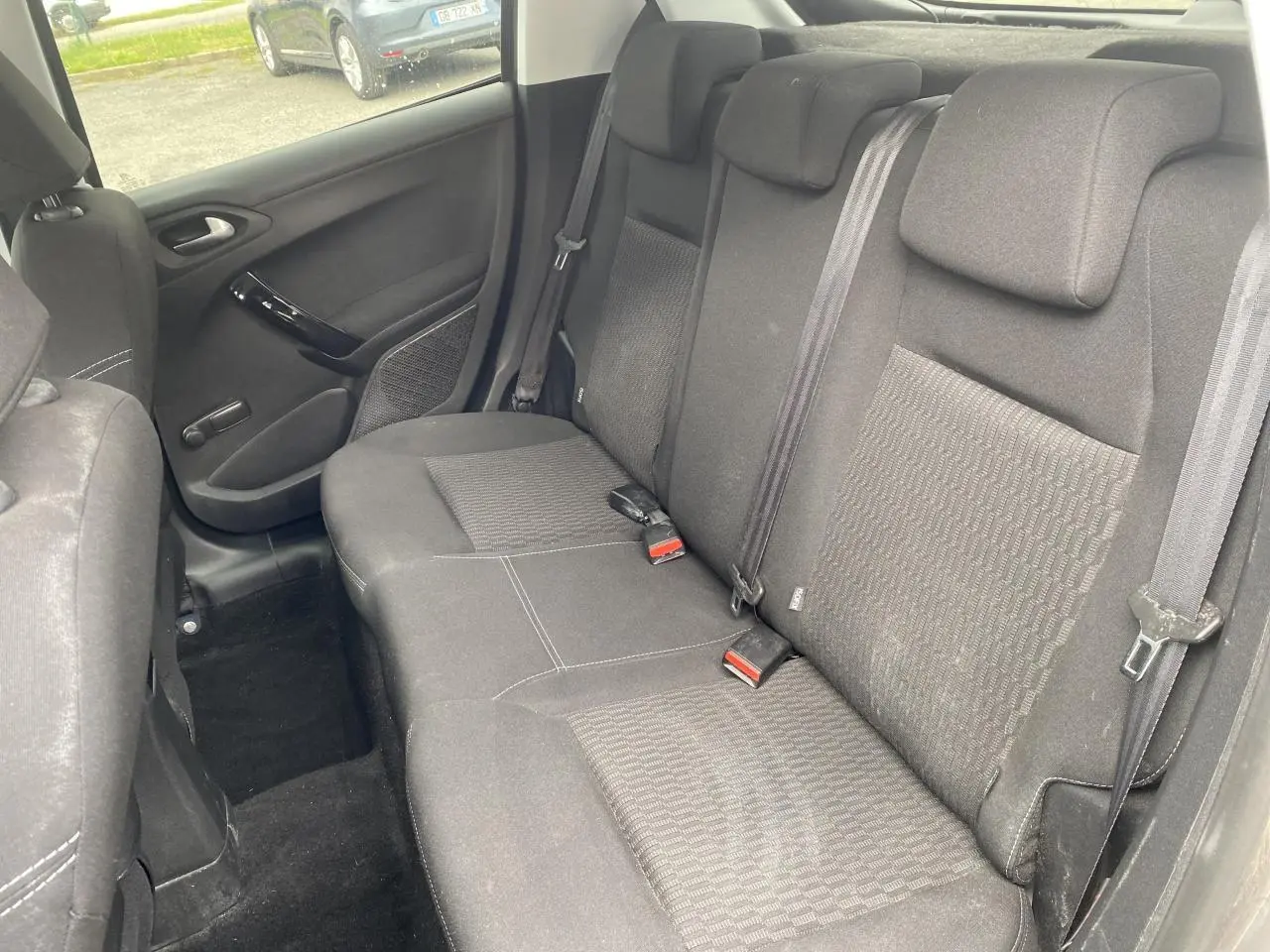 Vue intérieure de la banquette arrière en tissu gris foncé de la Peugeot 208 1.2i 2018, avec ceintures de sécurité visibles.