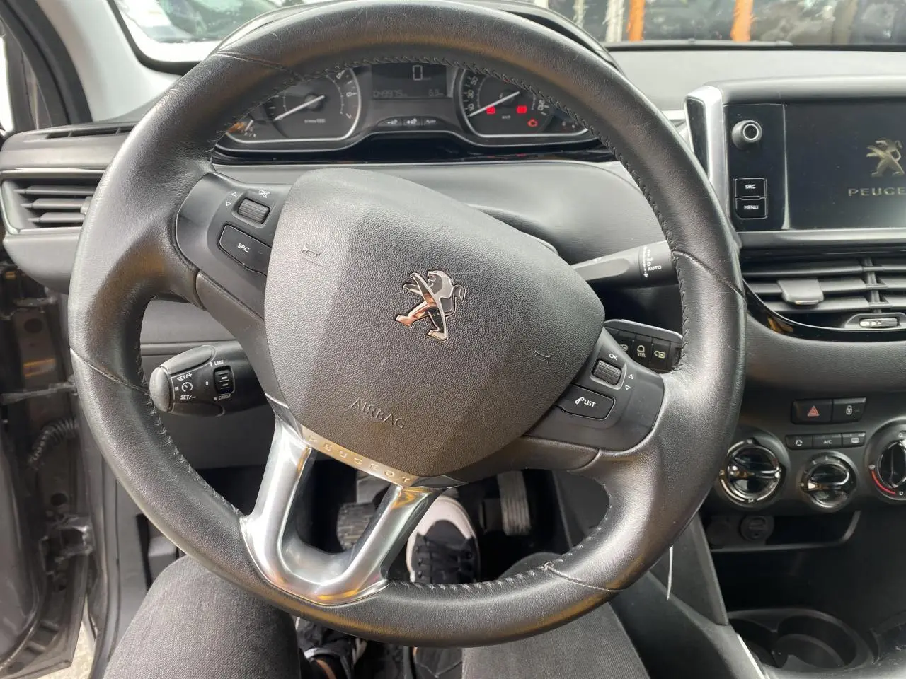 Vue rapprochée du volant cuir noir et du tableau de bord d'une Peugeot 208 gris métallisé de 2018 avec commandes intégrées.