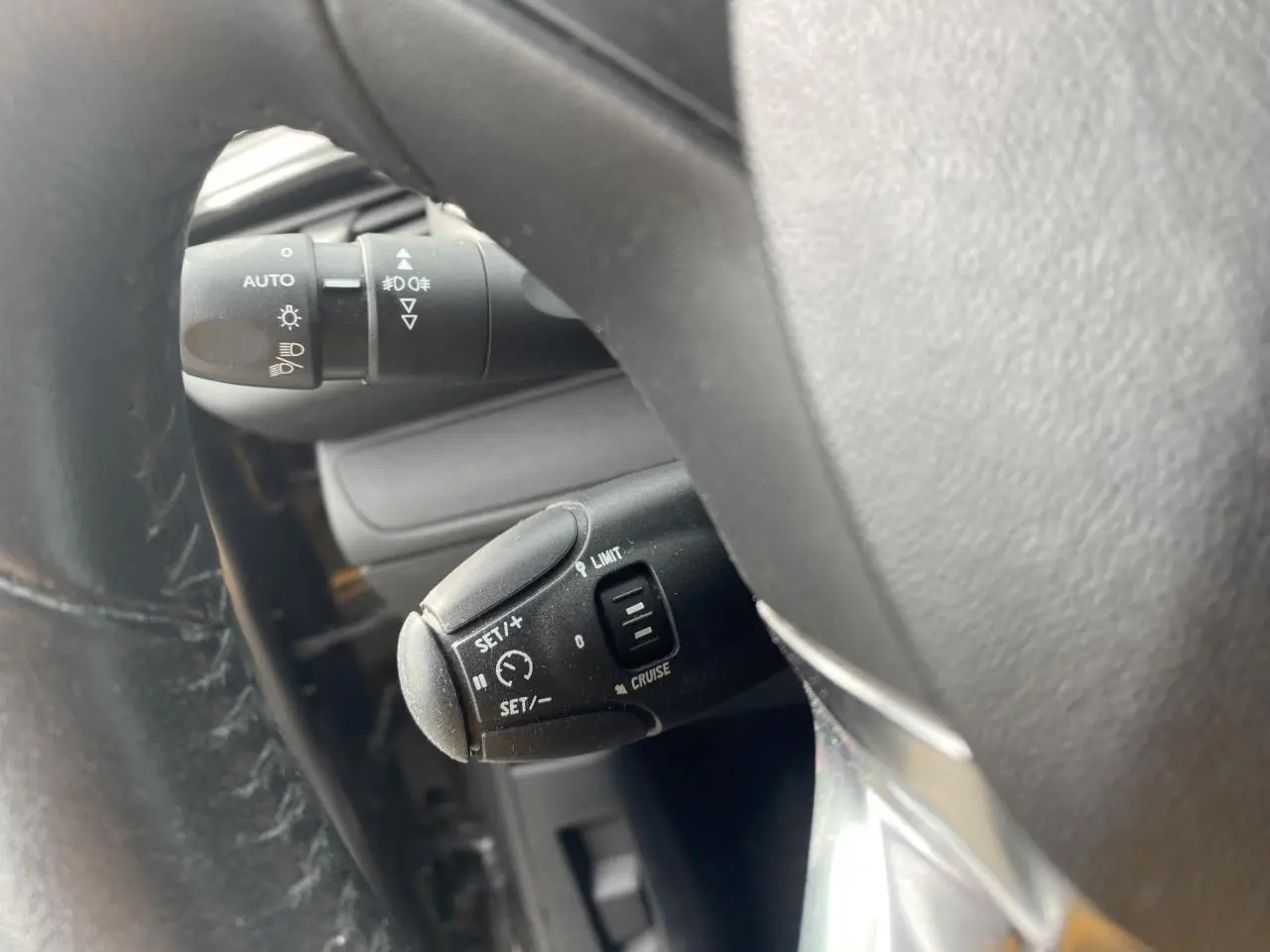 Gros plan sur la commande de régulateur de vitesse et allumage automatique des feux dans un Peugeot 208 gris, vue côté conducteur.