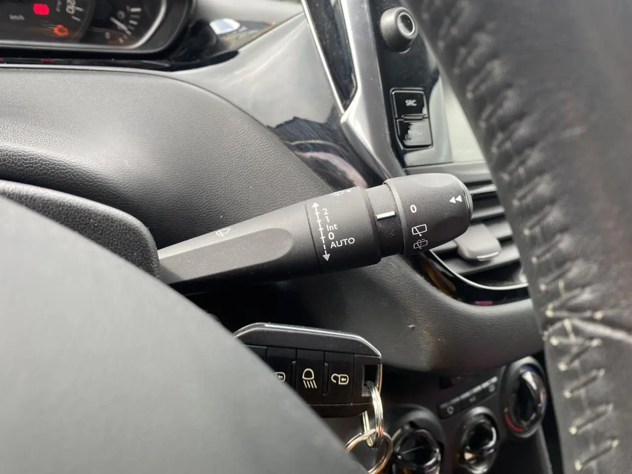 Gros plan sur la commande d’essuie-glace côté gauche du tableau de bord noir d’une Peugeot 208 gris métallisé.