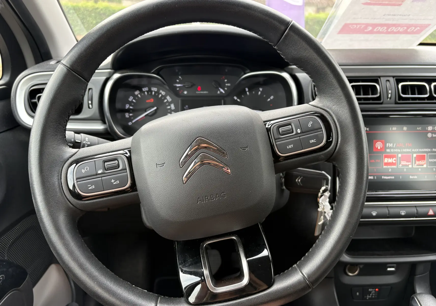Vue rapprochée du volant noir de la Citroën C3 beige 2019 avec commandes intégrées et tableau de bord visible.