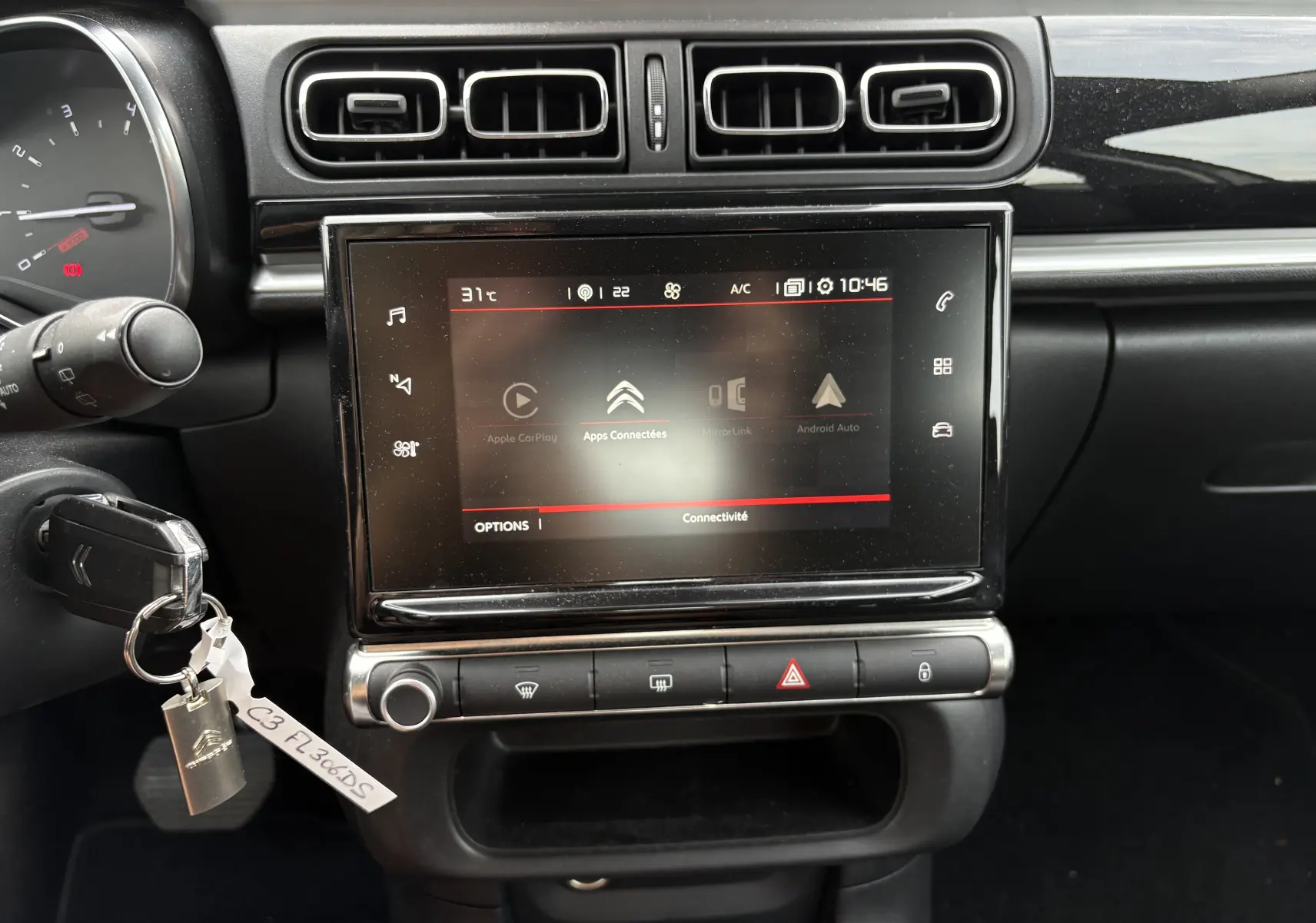 Vue rapprochée de l’écran tactile central et tableau de bord noir du Citroën C3 beige, avec commandes climatisation et clé insérée.