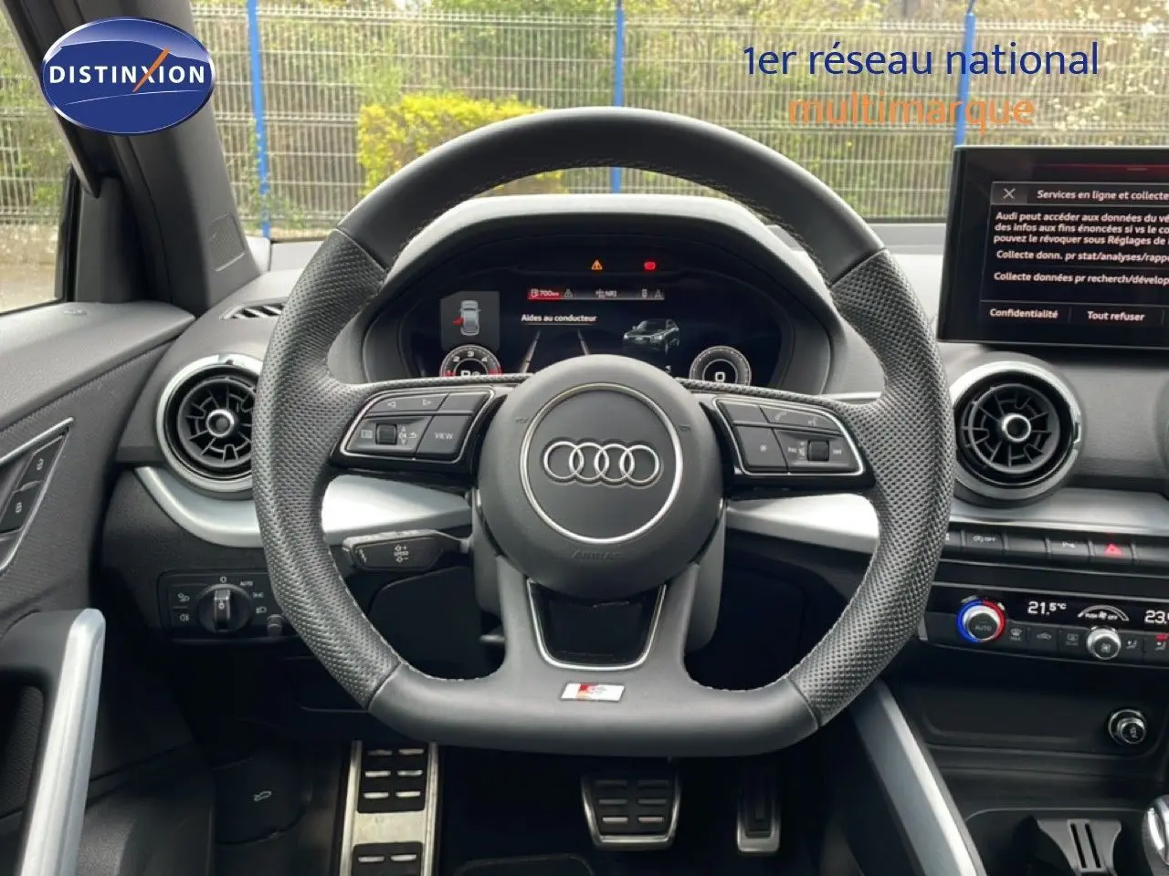 Vue intérieure centrée sur le volant sport perforé de l'Audi Q2 S-Line 2025 avec tableau de bord numérique et écran central.