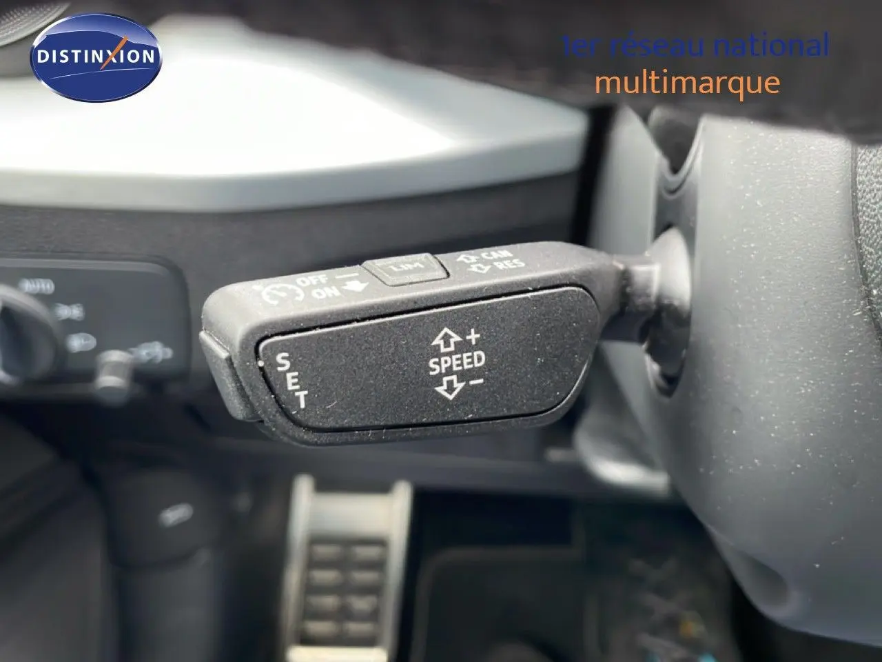 Gros plan sur la commande de régulateur de vitesse au volant d’un Audi Q2 noir mito metal, intérieur visible en arrière-plan.