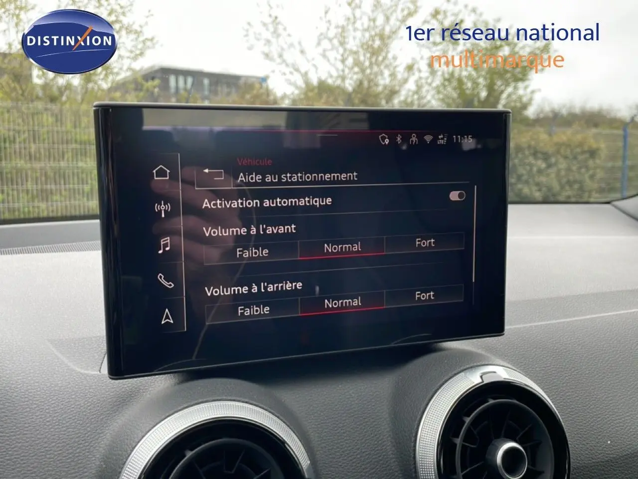 Écran central tactile de l’Audi Q2 2025 affichant les réglages d’aide au stationnement et volume sonore, intérieur noir.