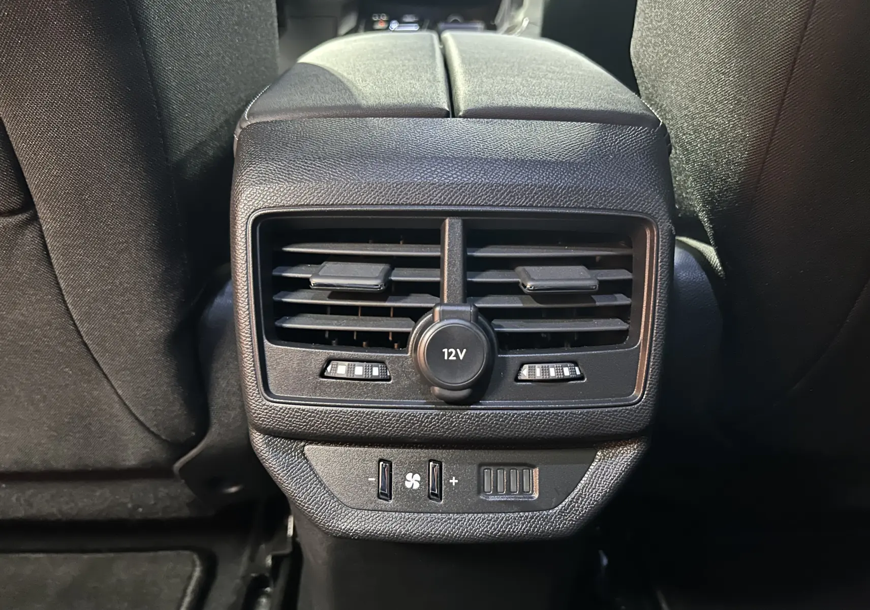 Vue rapprochée des aérateurs arrière et prise 12V noirs du Peugeot 5008 2024, entre les sièges arrière.