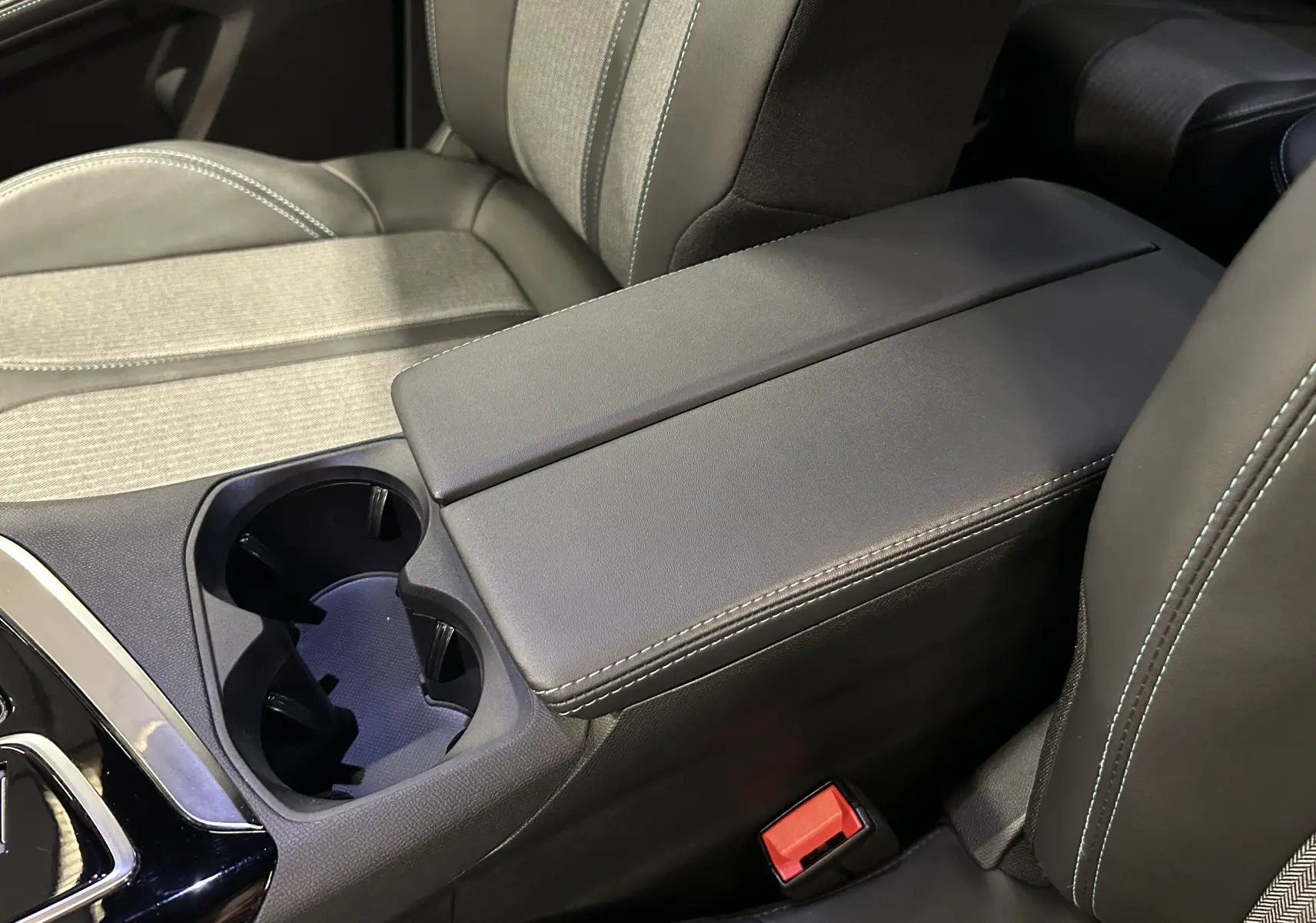 Gros plan sur l'accoudoir central et porte-gobelets entre les sièges avant en tissu et cuir gris du Peugeot 5008 2024.