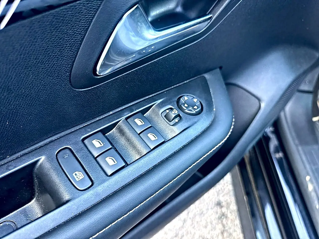 Détail de la porte côté conducteur noire d’une Peugeot 208 1.2 100 allure avec commandes des vitres et rétroviseurs électriques.