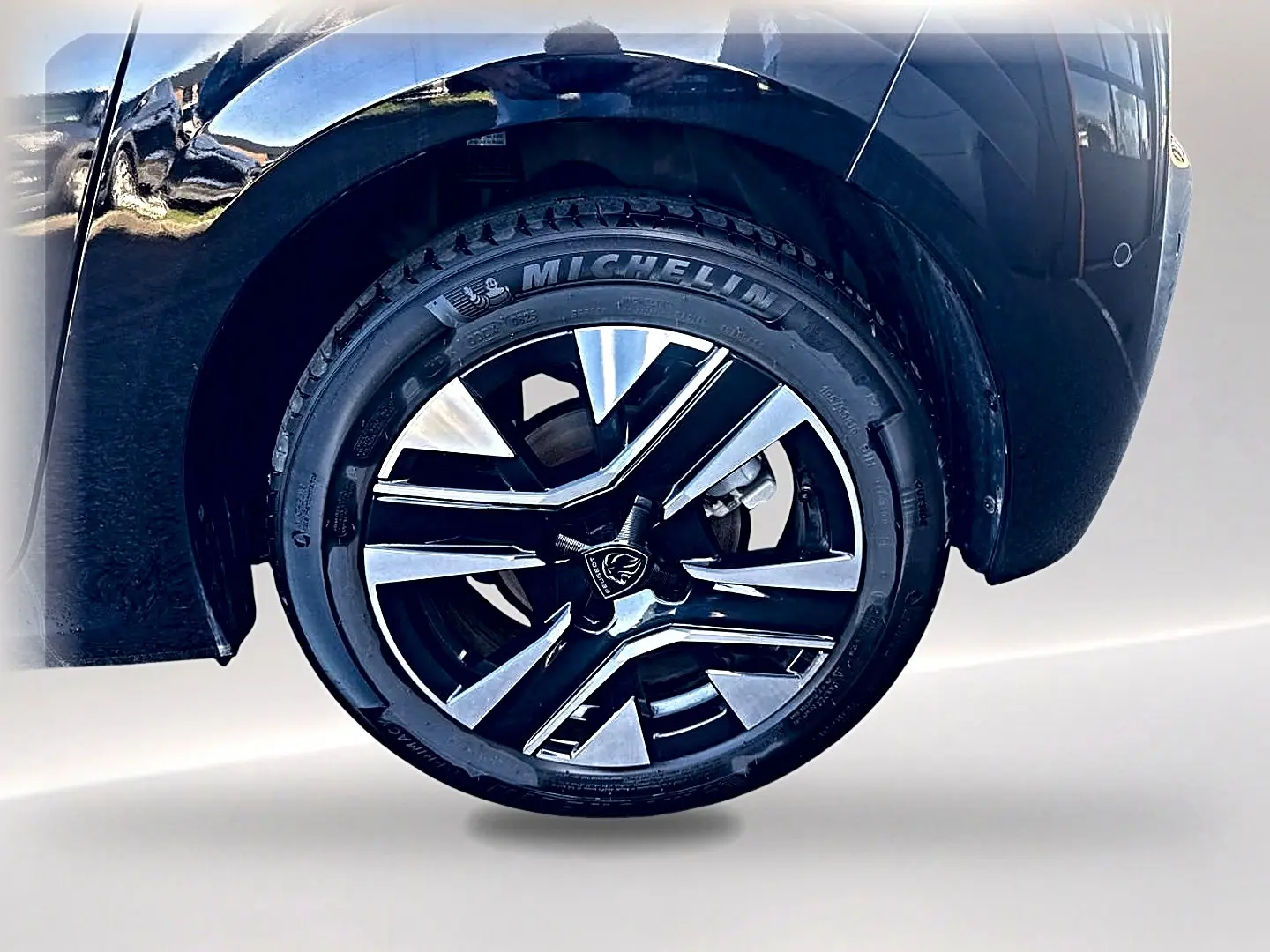 Gros plan sur la roue avant droite noire de la Peugeot 208 1.2 100 allure avec jante alu bicolore et pneu Michelin.