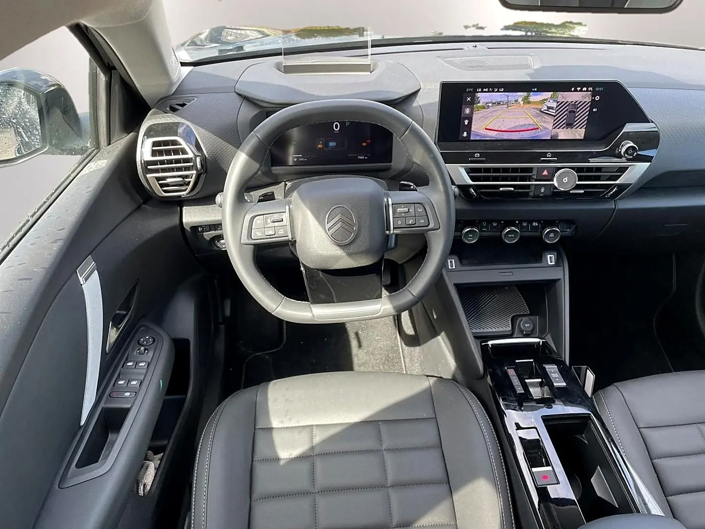 Vue intérieure avant centrée sur le volant cuir et l'écran tactile affichant la caméra de recul du Citroën C4 X noir 2025.