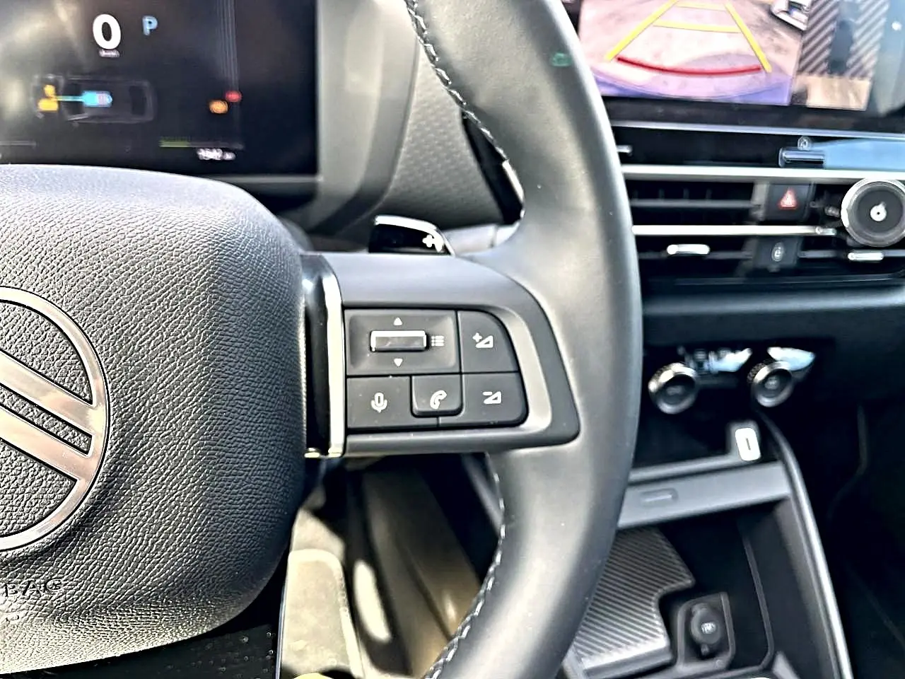 Vue rapprochée du volant cuir noir de la Citroën C4 X 2025 avec commandes vocales et écran tactile en arrière-plan.