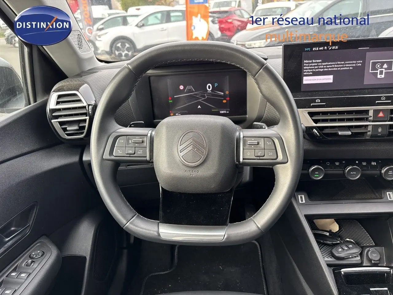 Vue intérieure centrée sur le volant cuir noir d’une Citroën C4 hybride 2025 avec tableau de bord digital et écran tactile.