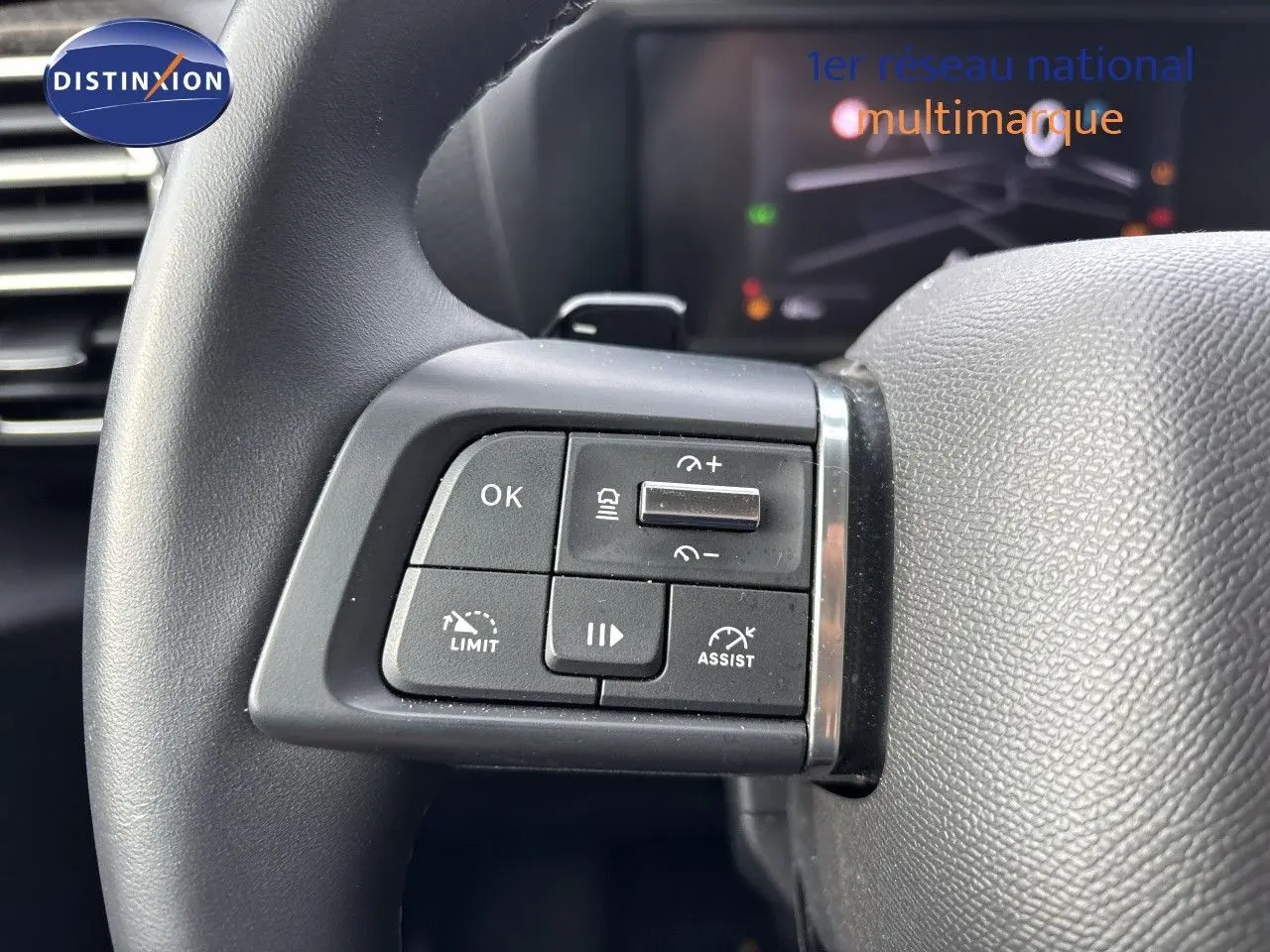 Gros plan sur les commandes au volant côté gauche d’un Citroën C4 blanc Okenite Metal, avec boutons de régulateur et assistance.