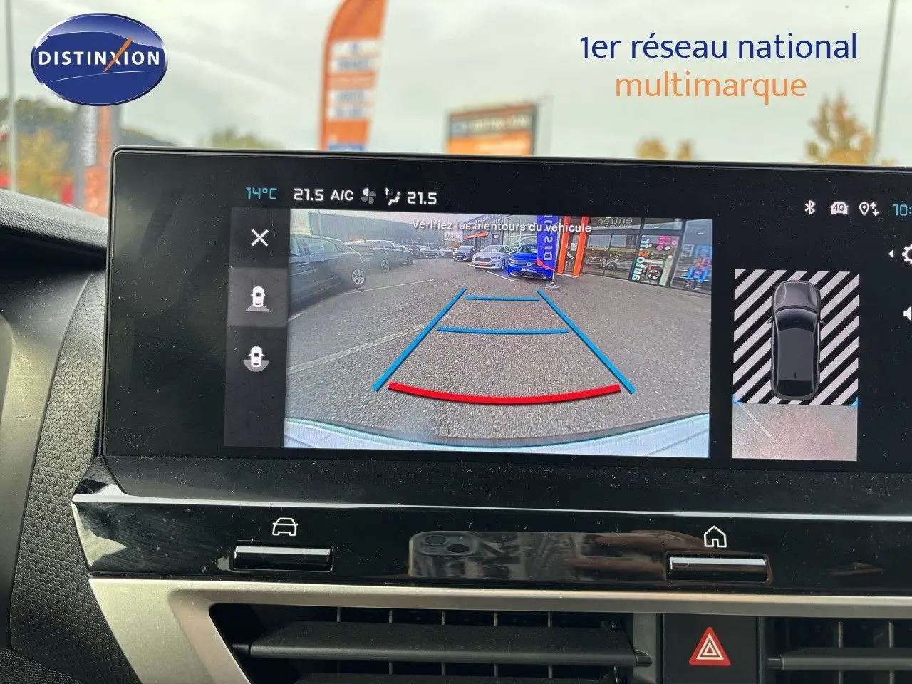 Écran intérieur montrant la caméra de recul d'une Citroën C4 blanc Okenite, vue arrière avec lignes de guidage colorées.