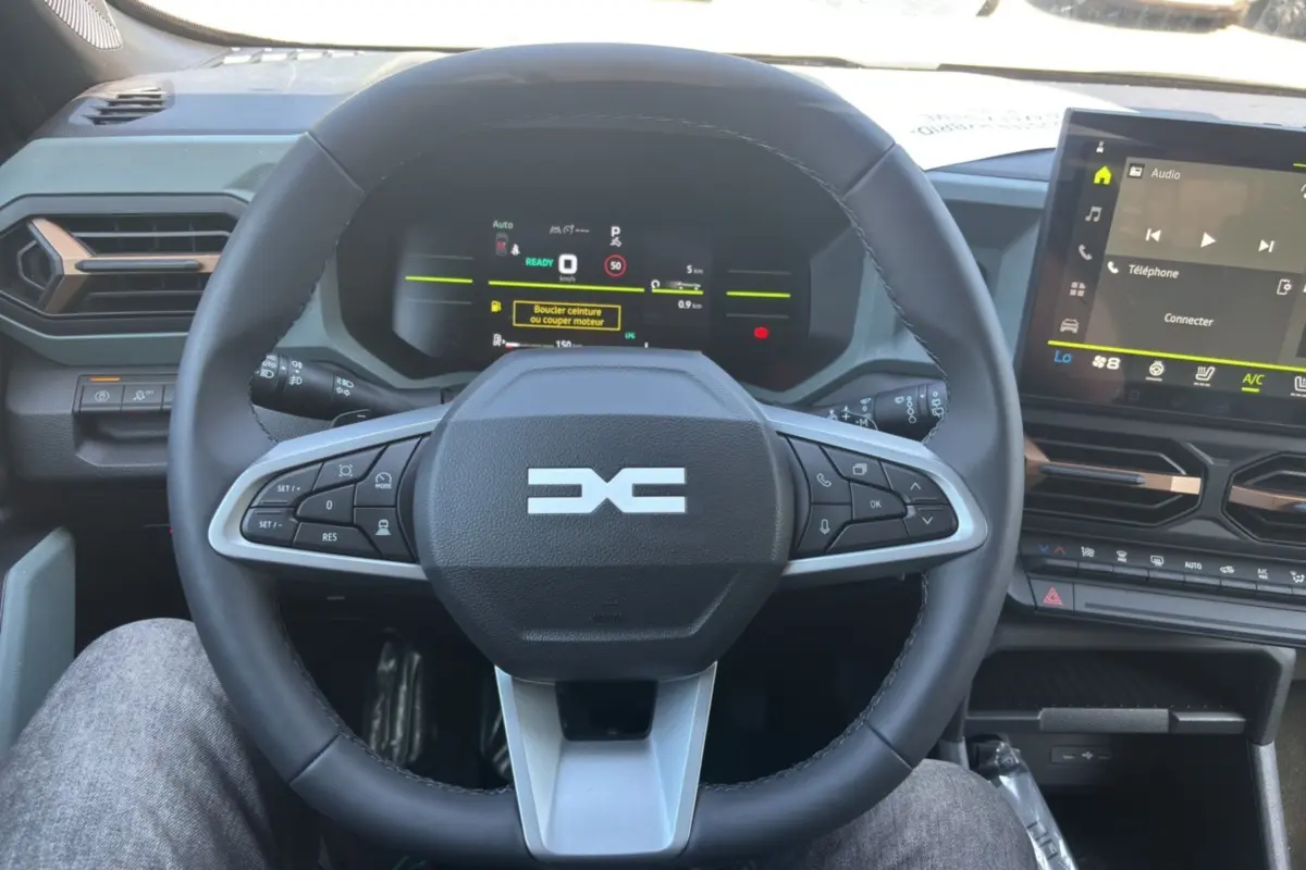 Vue centrée sur le volant cuir du Dacia Duster Hybrid-G 150 4x4, avec tableau de bord numérique et écran tactile visible.