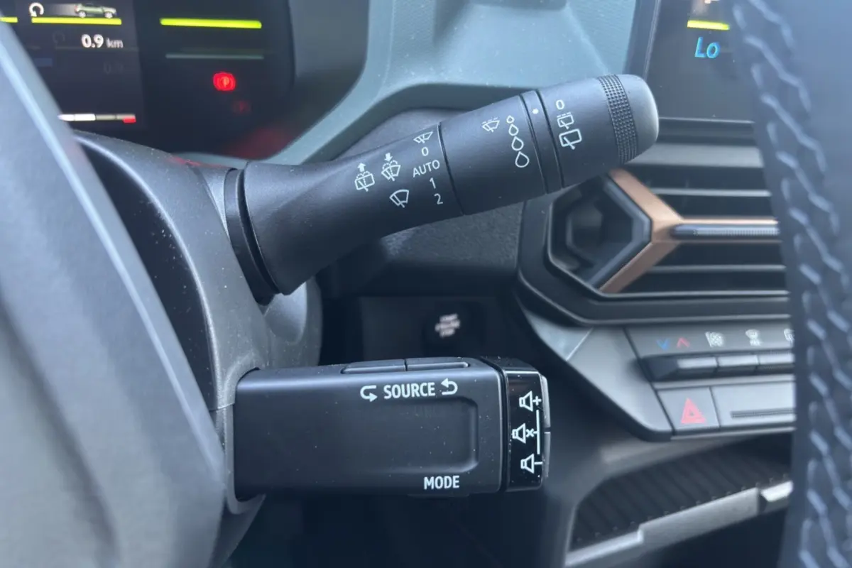 Gros plan sur les commandes au volant du Dacia Duster Hybrid-G 150 4x4, avec tableau de bord et aérateurs noirs et bronze.
