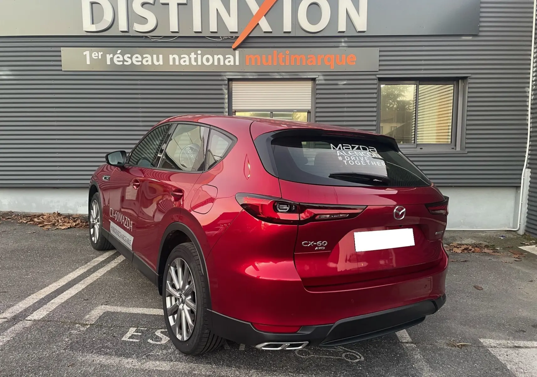 Vue 3/4 arrière droite d'un Mazda CX-60 Soul Red Crystal garé devant un bâtiment Distinxion.
