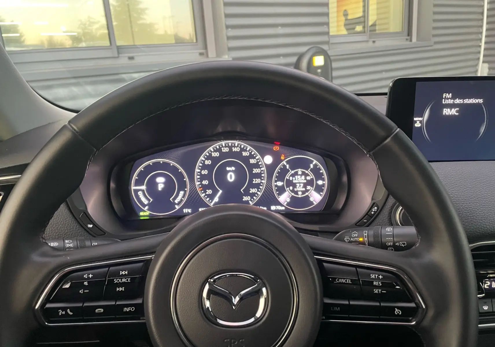 Vue depuis le siège conducteur sur le volant noir Mazda CX-60 et le tableau de bord numérique allumé.