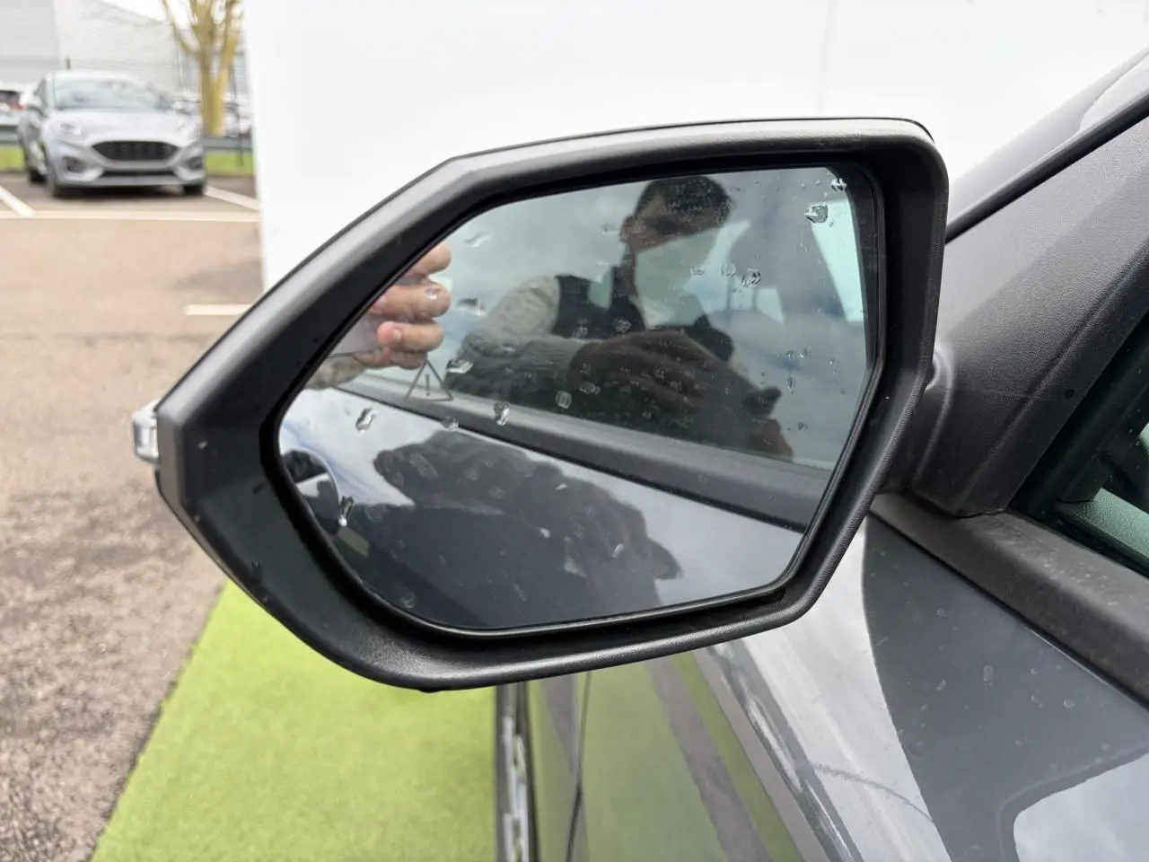 Rétroviseur extérieur côté gauche du Hyundai Kona 2026 en gris métallisé Ecotronic, avec reflet et gouttes d'eau visibles.